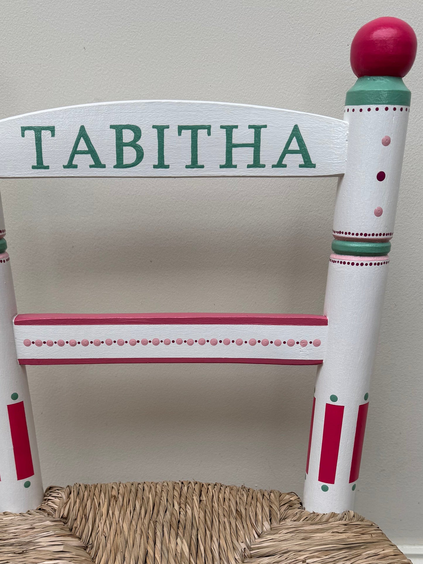 Children's chair with a woven seat and 'Tabitha' on the backrest against a white wall.