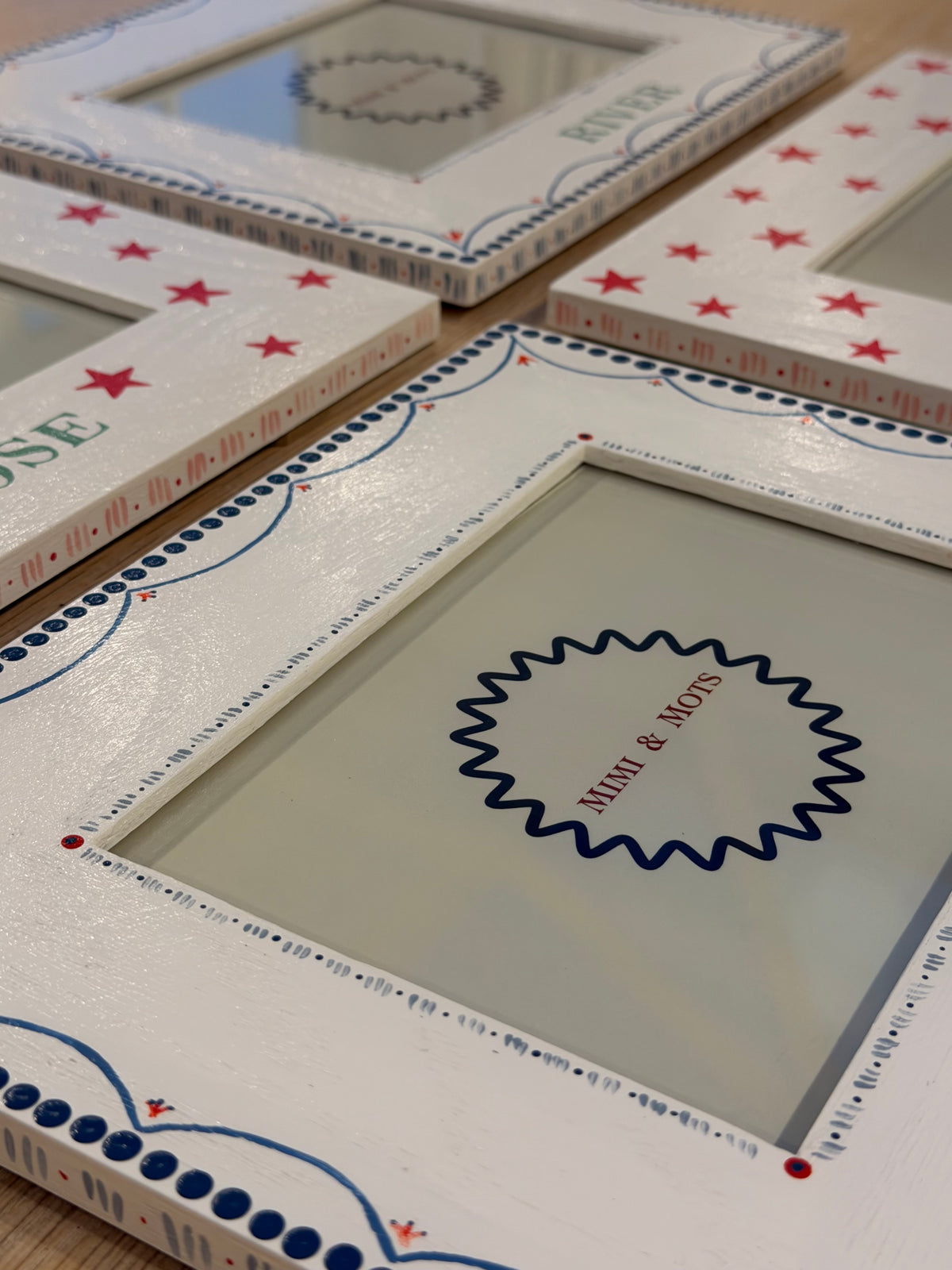 A close-up of a white decorative picture frame with red stars, blue dotted borders, and a central blue scalloped circle containing the text 'Miki & Mavis'.