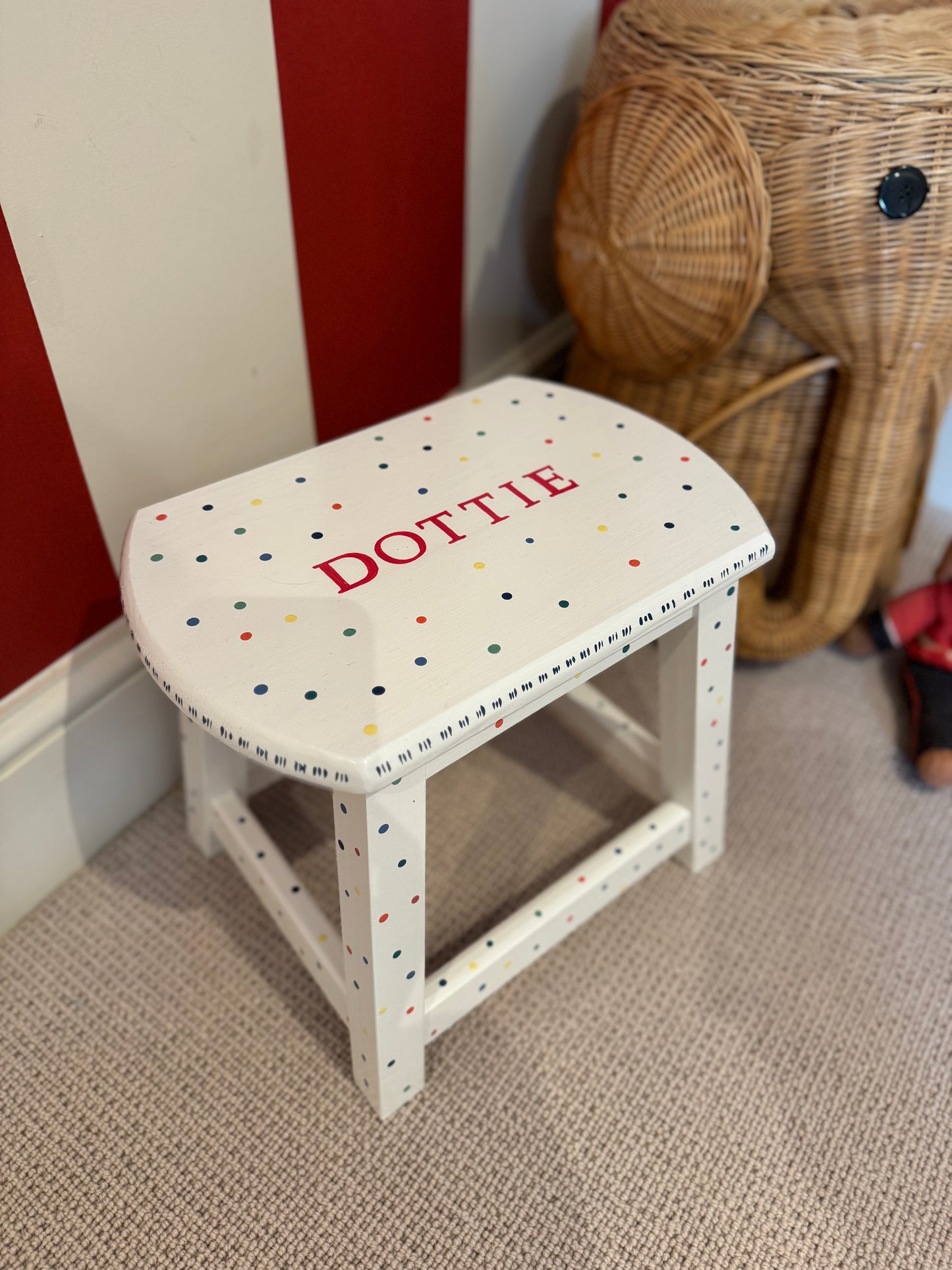 White stool with polka dot pattern and 'DOTTIE' text against a red and white wall.