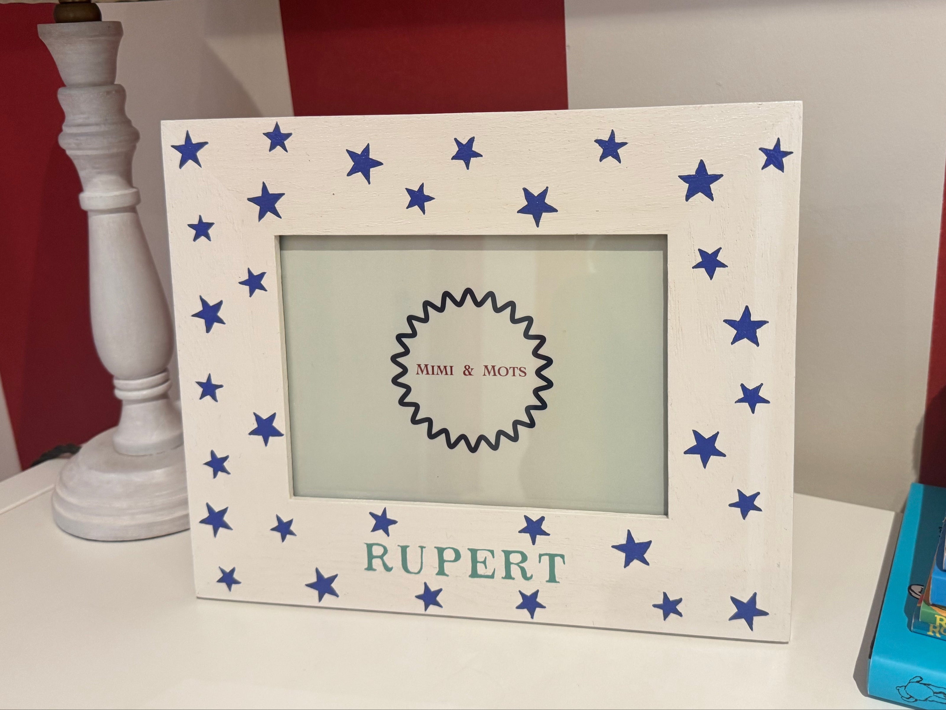 White photo frame with blue stars, lamp, and books on a shelf