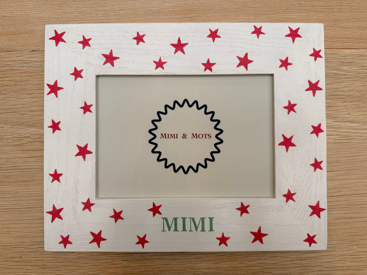 A square white wooden picture frame decorated with pink stars and the name 'MIMI' in green on the left side, shown on a light wood background.